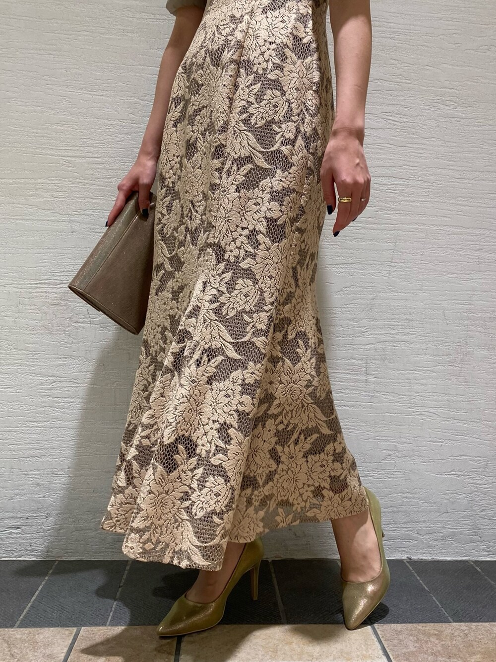 ベージュ系のドレス、ゴールド系のクラッチバッグ、ゴールド系のパンプスを着用したレディースの秋コーディネートの2枚目の写真