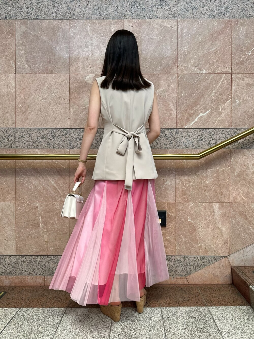 ベージュ系のベスト、ホワイト系のハンドバッグ、ピンク系のスカートを着用したレディースの夏コーディネートの5枚目の写真