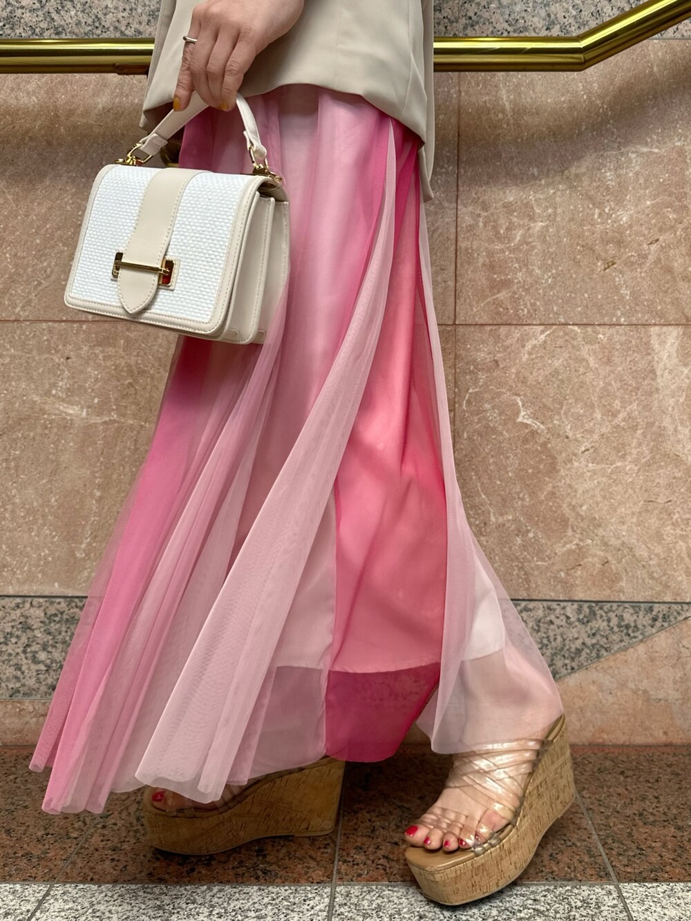 ベージュ系のベスト、ホワイト系のハンドバッグ、ピンク系のスカートを着用したレディースの夏コーディネートの10枚目の写真