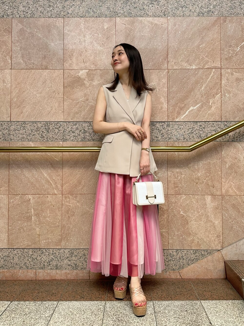 ベージュ系のベスト、ホワイト系のハンドバッグ、ピンク系のスカートを着用したレディースの夏コーディネートの2枚目の写真