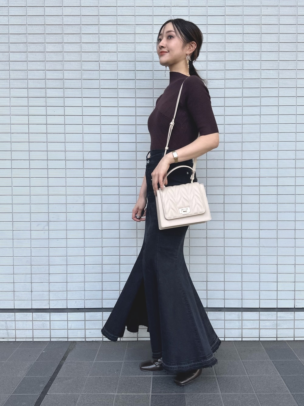 ブラウン系のニット/セーター、ブラック系のデニムスカート、ベージュ系のショルダーバッグを着用したレディースの秋コーディネートの2枚目の写真