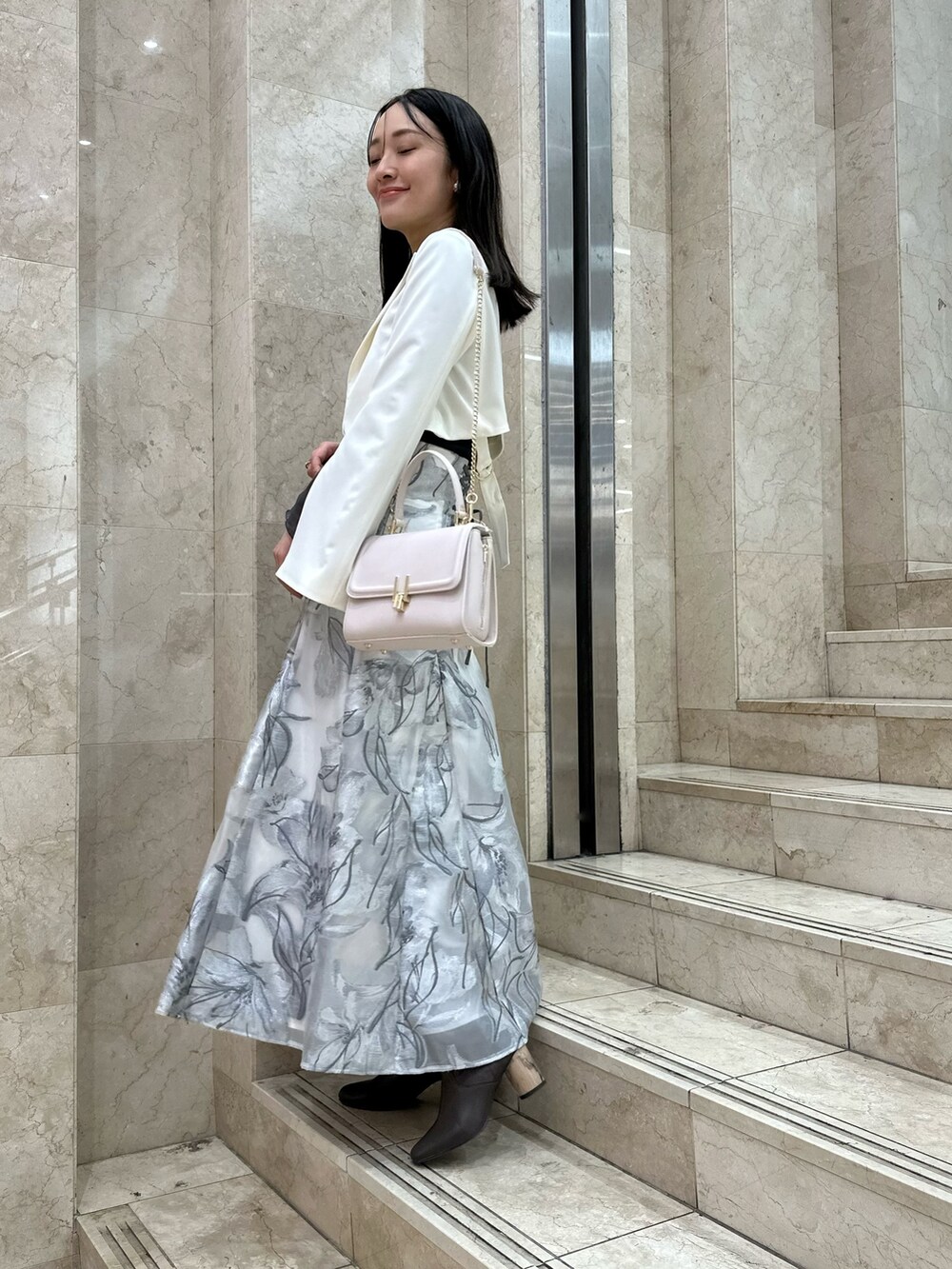 ホワイト系のテーラードジャケット、グレー系のスカート、グレー系のニット/セーターを着用したレディースの春コーディネートの2枚目の写真