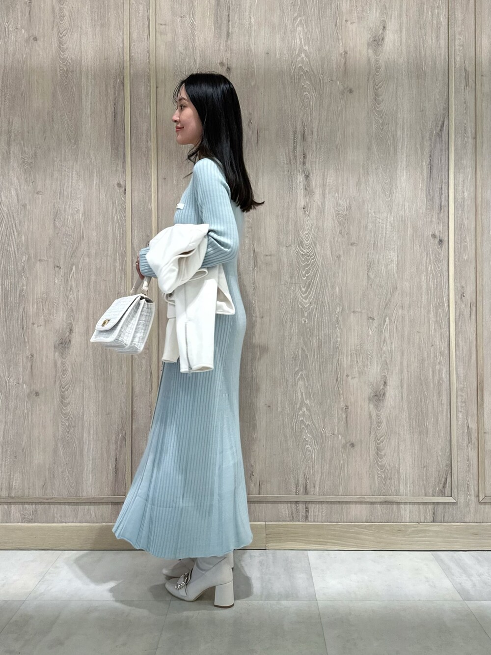 ホワイト系のハンドバッグ、ホワイト系のブーツ、ブルー系のワンピースを着用したレディースの冬コーディネートの4枚目の写真