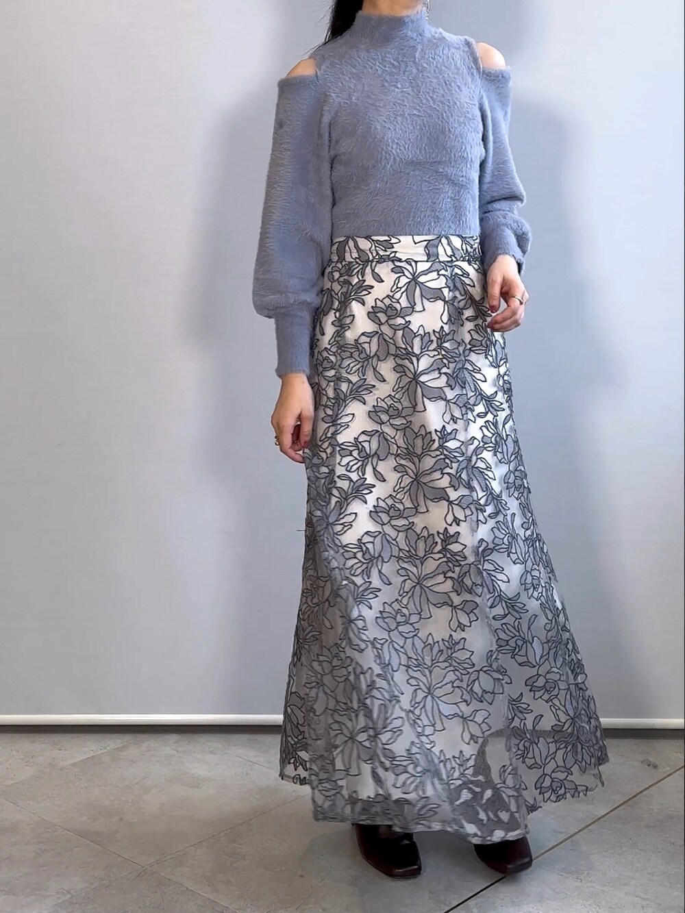 ブルー系のニット/セーター、グレー系のスカート、ブラウン系のブーツを着用したレディースの秋コーディネートの2枚目の写真