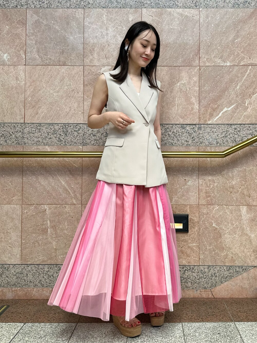 ベージュ系のベスト、ホワイト系のハンドバッグ、ピンク系のスカートを着用したレディースの夏コーディネートの3枚目の写真