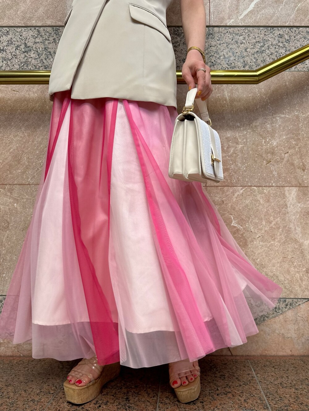 ベージュ系のベスト、ホワイト系のハンドバッグ、ピンク系のスカートを着用したレディースの夏コーディネートの9枚目の写真