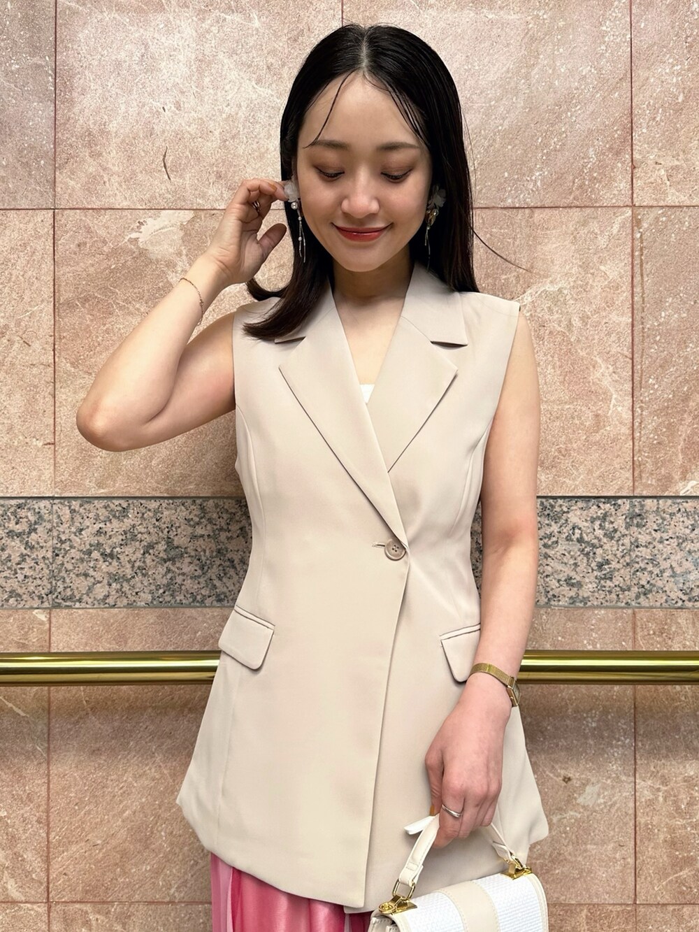 ベージュ系のベスト、ホワイト系のハンドバッグ、ピンク系のスカートを着用したレディースの夏コーディネートの6枚目の写真