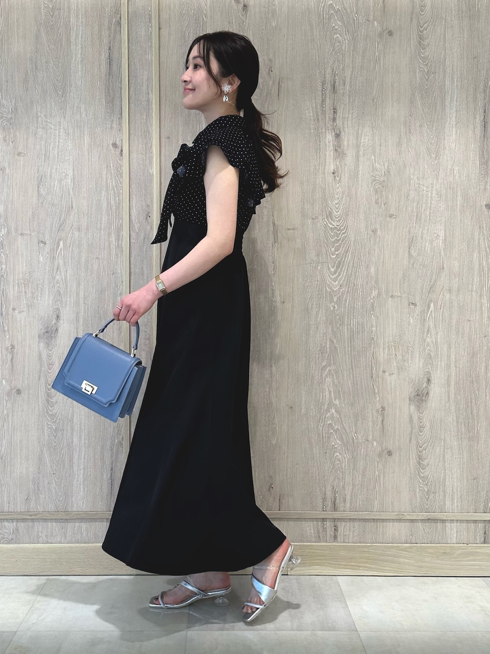 ブラック系のワンピース、ブルー系のハンドバッグ、シルバー系のサンダルを着用したレディースの春コーディネートの3枚目の写真