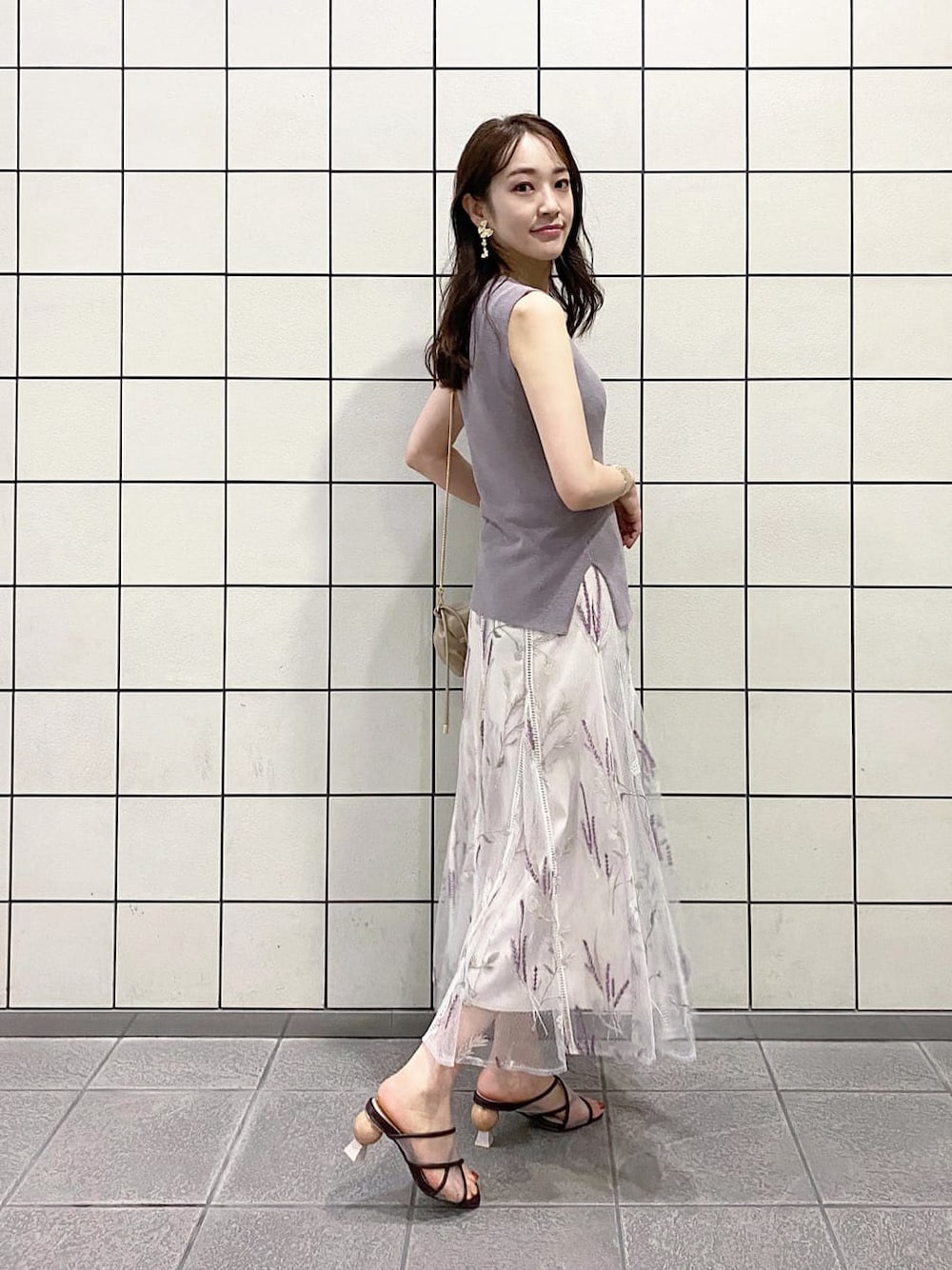 ベージュ系のクラッチバッグ、ブラウン系のサンダル、ホワイト系のスカートを着用したレディースの夏コーディネートの2枚目の写真