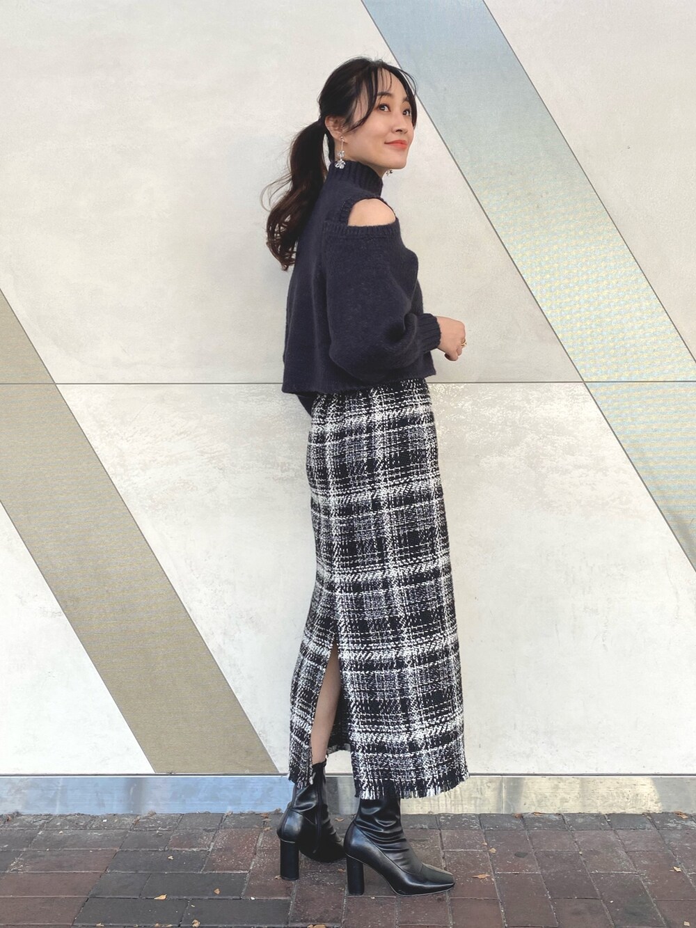 グレー系のニット/セーター、ブラック系のスカート、ブラック系のブーツを着用したレディースの秋コーディネートの2枚目の写真