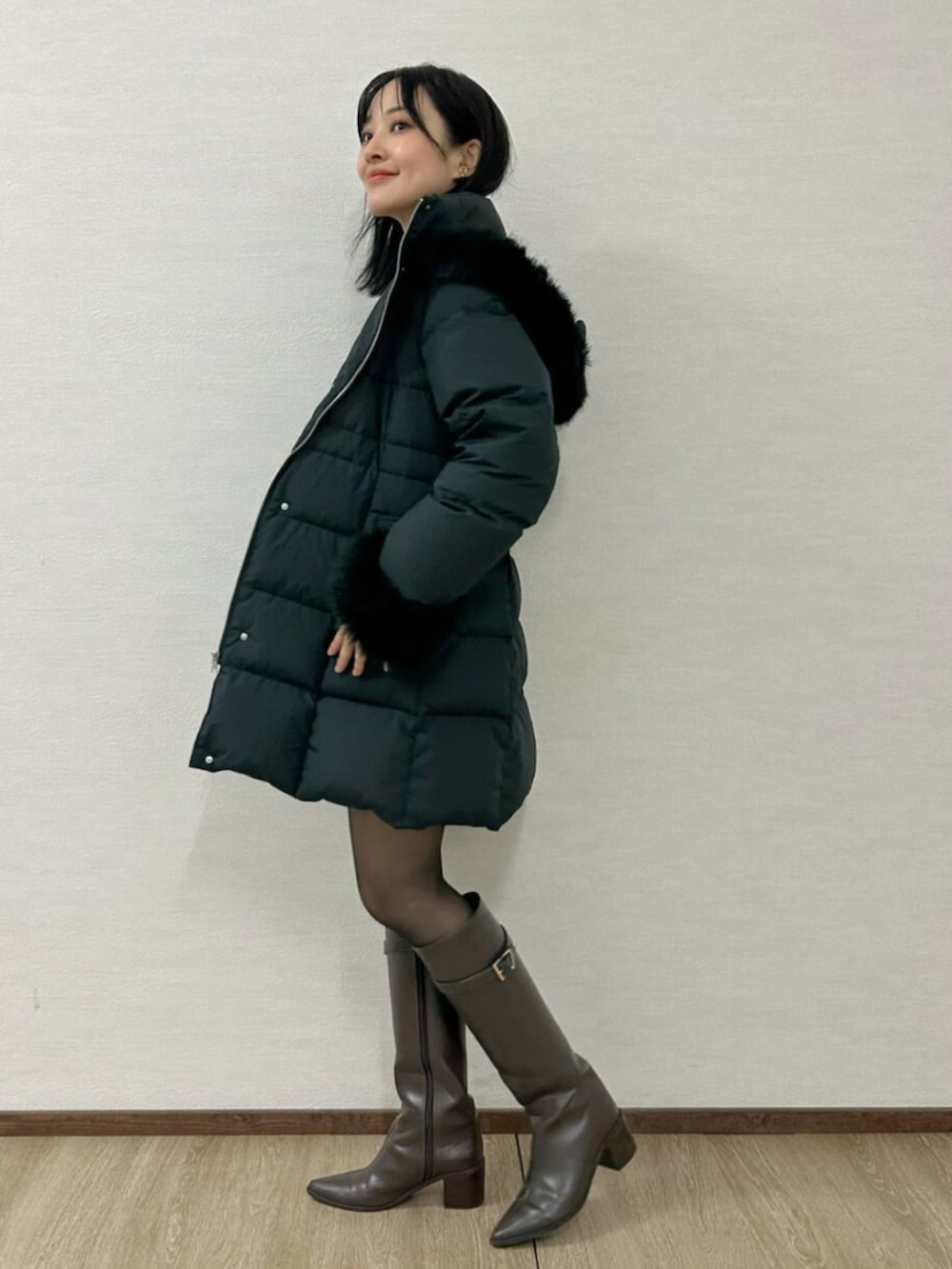 グリーン系のワンピース、ブラウン系のブーツ、ブラック系のダウンジャケット/コートを着用したレディースの冬コーディネートの2枚目の写真