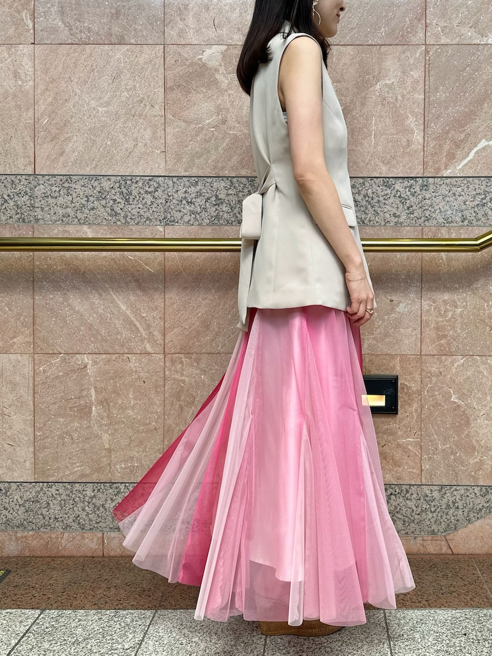 ベージュ系のベスト、ホワイト系のハンドバッグ、ピンク系のスカートを着用したレディースの夏コーディネートの4枚目の写真