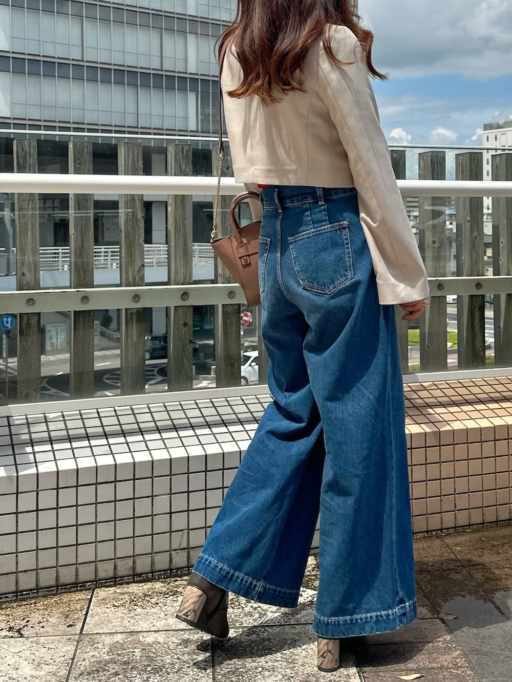 ブルー系のデニムパンツ、ブラウン系のブーツ、ブラウン系のハンドバッグを着用したレディースの夏コーディネートの4枚目の写真