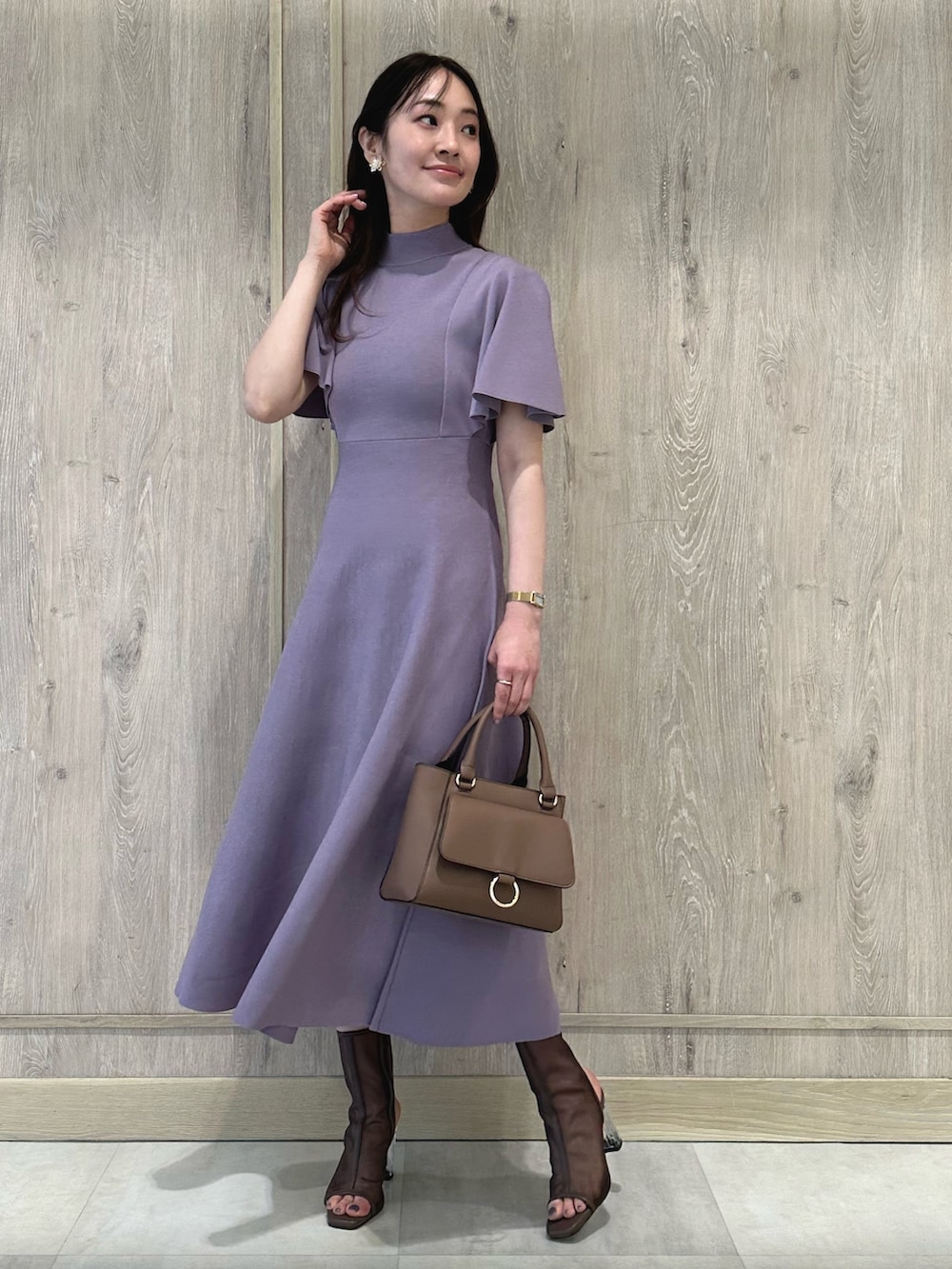 ブラウン系のハンドバッグ、ブラウン系のブーツ、パープル系のワンピースを着用したレディースの春コーディネートの3枚目の写真