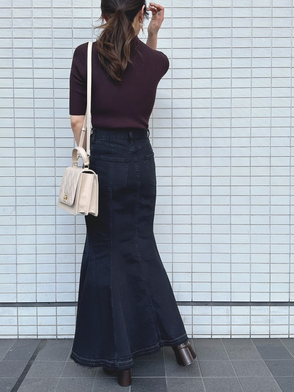 ブラウン系のニット/セーター、ブラック系のデニムスカート、ベージュ系のショルダーバッグを着用したレディースの秋コーディネートの3枚目の写真