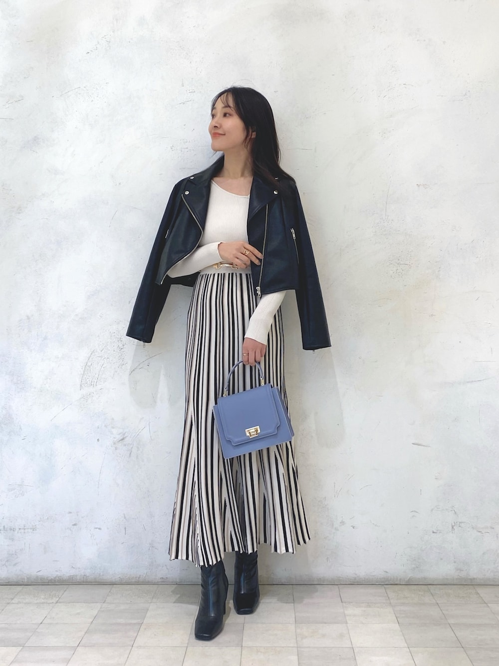 ブルー系のハンドバッグ、ブラック系のライダースジャケット、ホワイト系のワンピースを着用したレディースの冬コーディネートの2枚目の写真