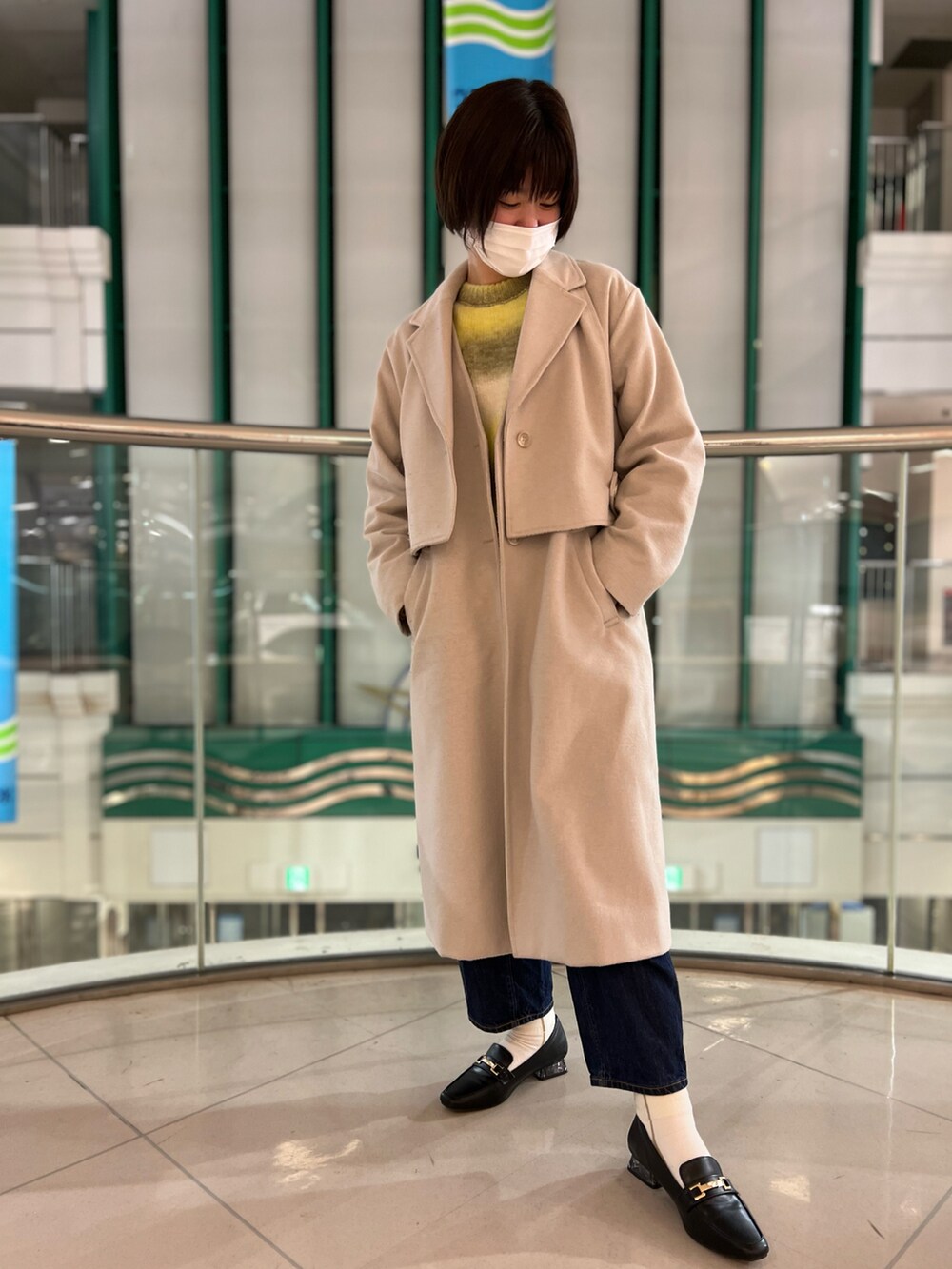 イエロー系のニット/セーター、ベージュ系のノーカラーコート、ブルー系のデニムパンツを着用したレディースの冬コーディネートの2枚目の写真