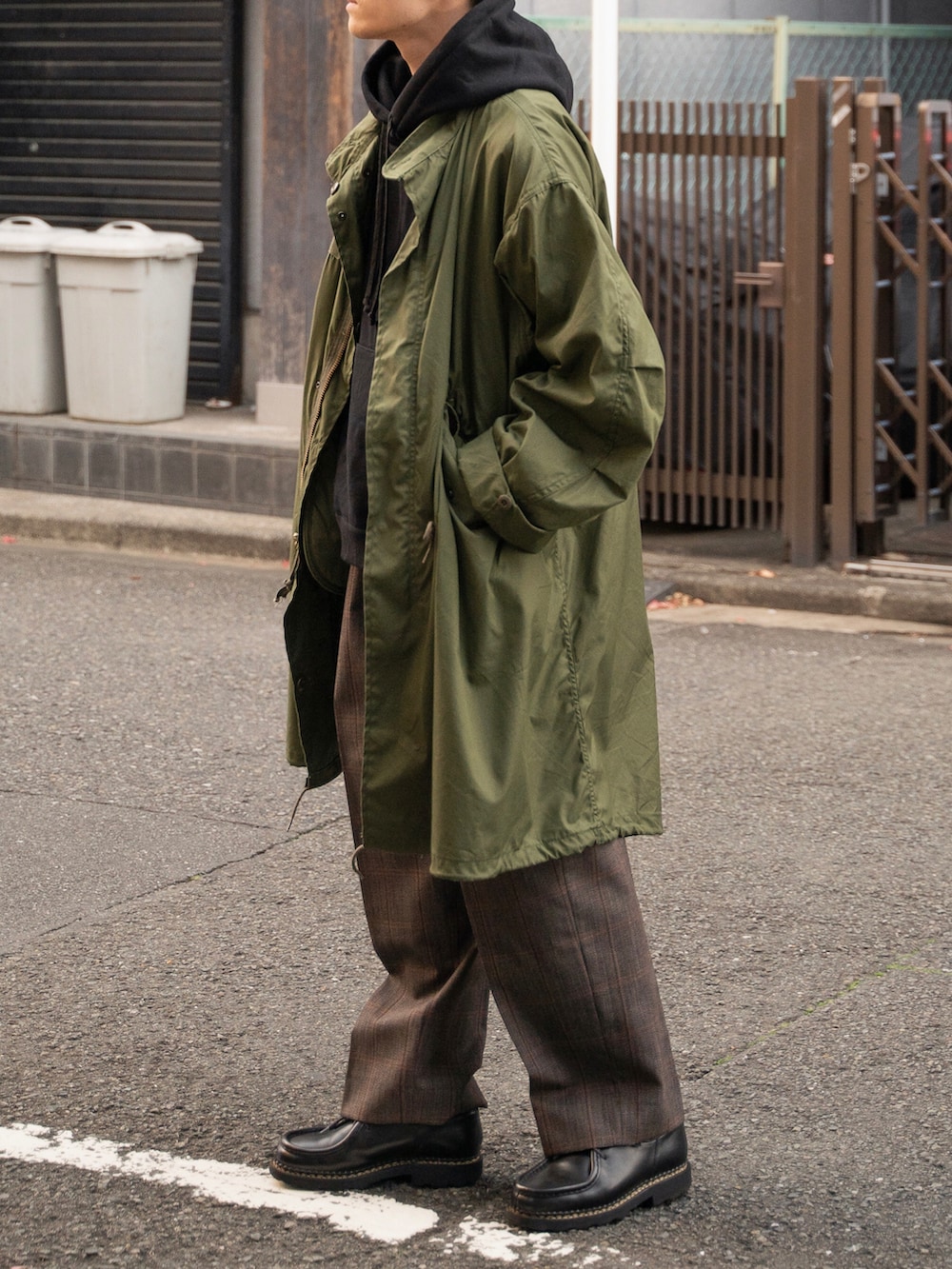 グリーン系のモッズコート、ブラウン系のその他パンツ、ブラック系のパーカーを着用したメンズの冬コーディネートの2枚目の写真