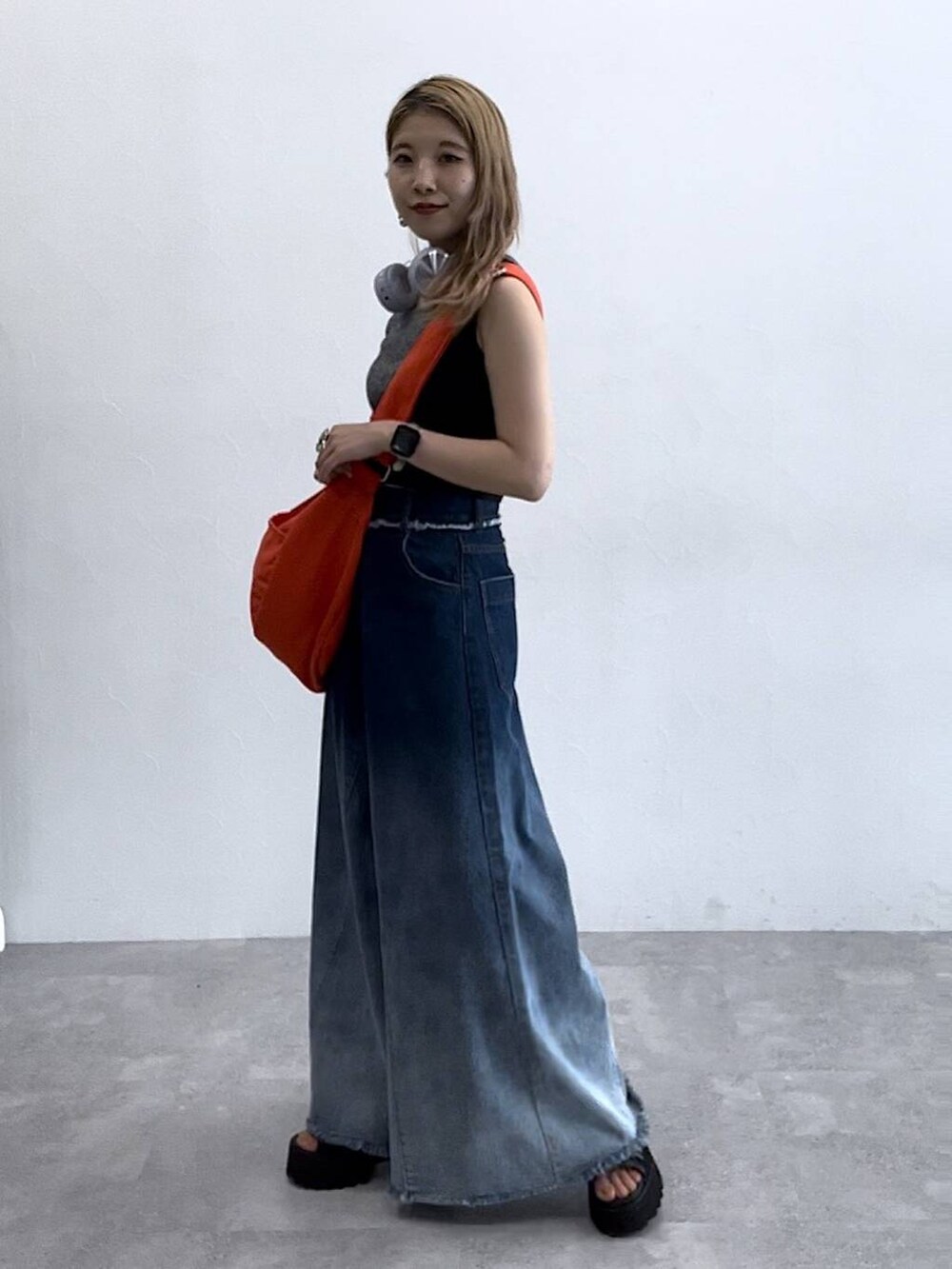 ブルー系のデニムパンツ、ブラック系のタンクトップ、オレンジ系のショルダーバッグを着用したレディースの夏コーディネートの3枚目の写真