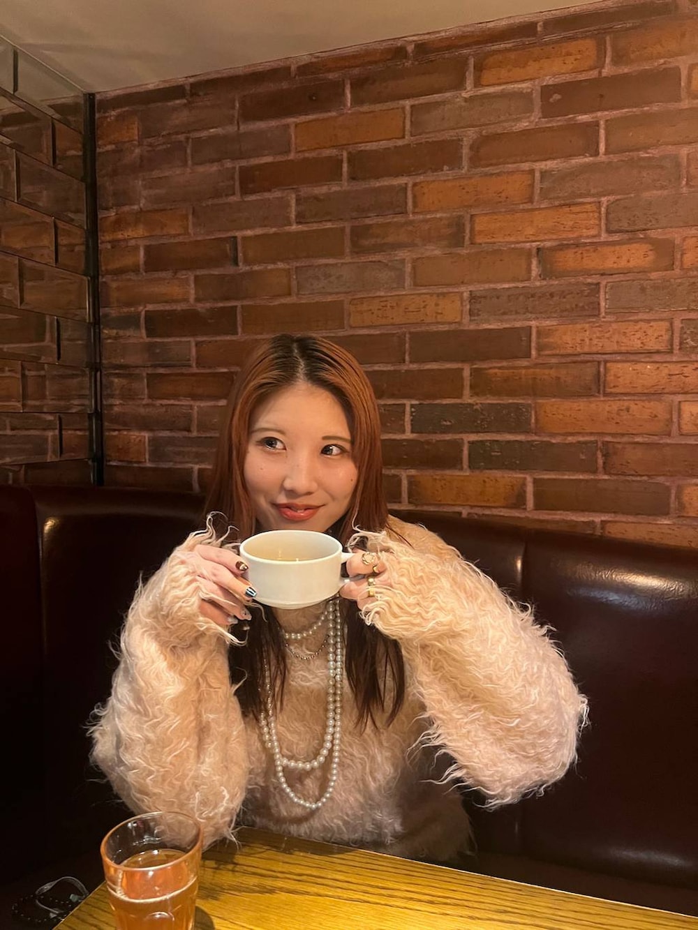 オレンジ系のカーディガン/ボレロ、ベージュ系のネックレスを着用したレディースの冬コーディネートの2枚目の写真