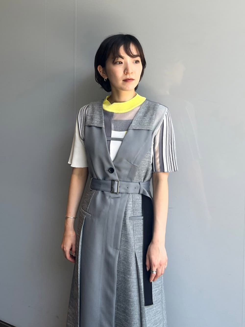 グレー系のジャンパースカート、イエロー系のニット/セーターを着用したレディースの夏コーディネートの3枚目の写真