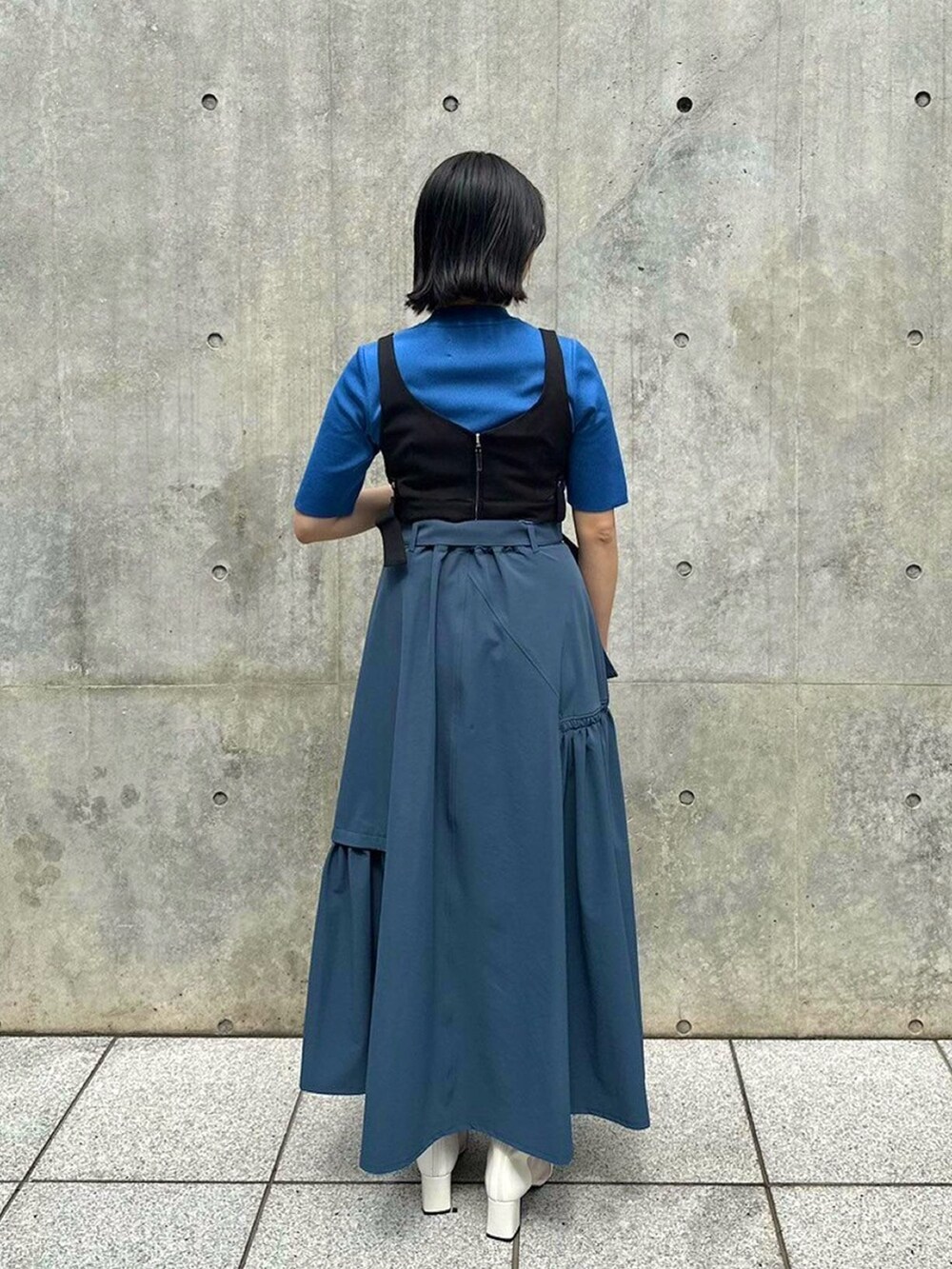 ブルー系のニット/セーター、ブラック系のベスト、グレー系のスカートを着用したレディースの春コーディネートの3枚目の写真