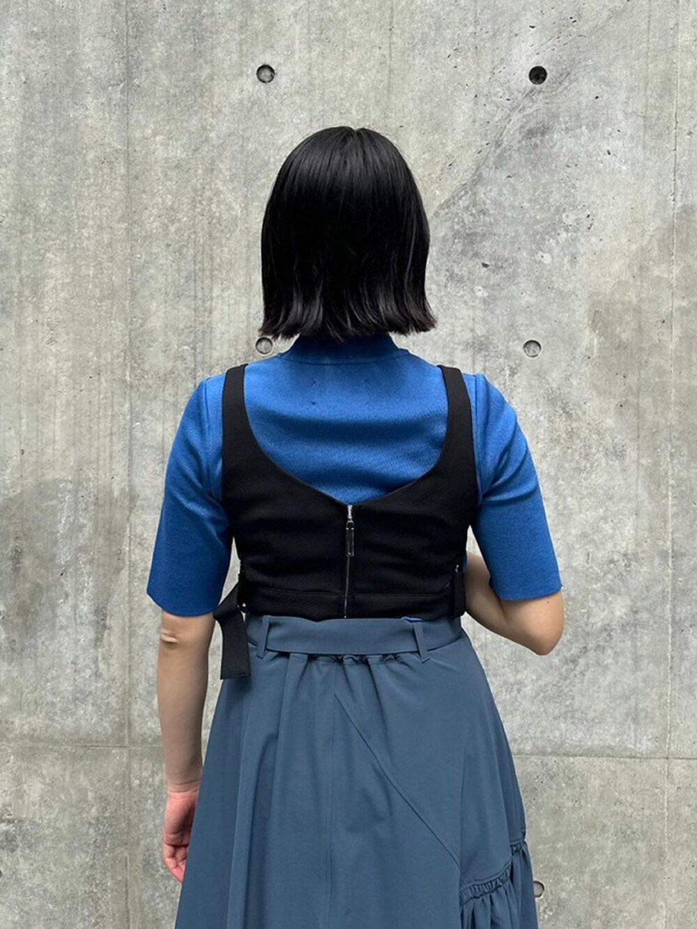 ブルー系のニット/セーター、ブラック系のベスト、グレー系のスカートを着用したレディースの春コーディネートの6枚目の写真