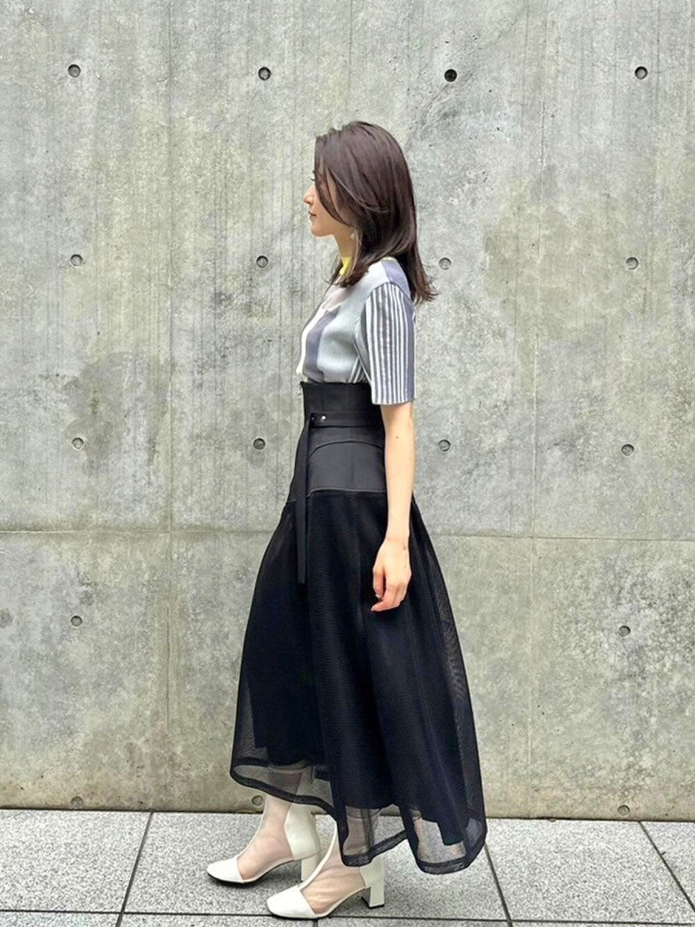 イエロー系のニット/セーター、ブラック系のスカートを着用したレディースの春コーディネートの2枚目の写真