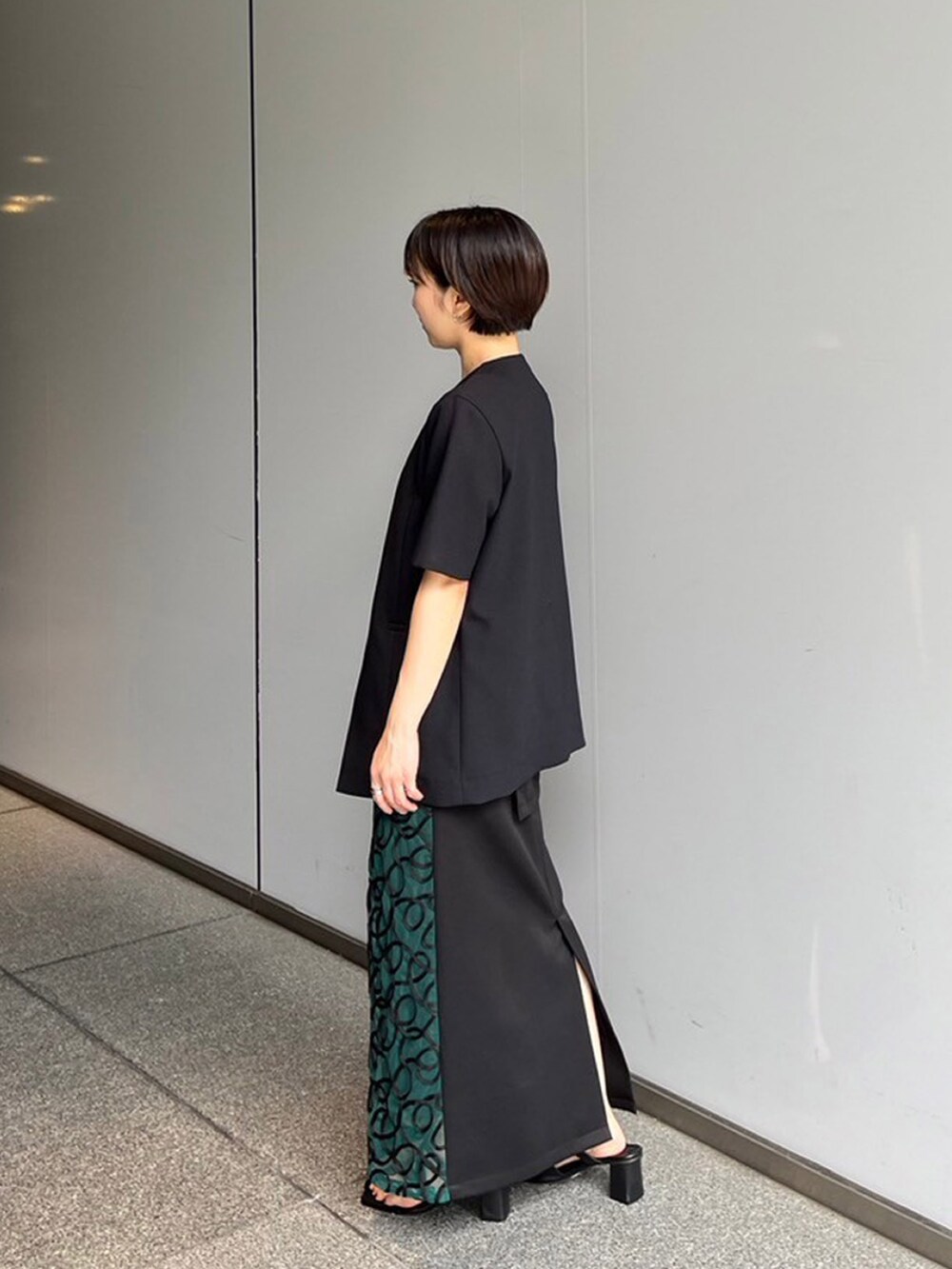 ブラック系のノーカラージャケット、グリーン系のスカートを着用したレディースの夏コーディネートの2枚目の写真