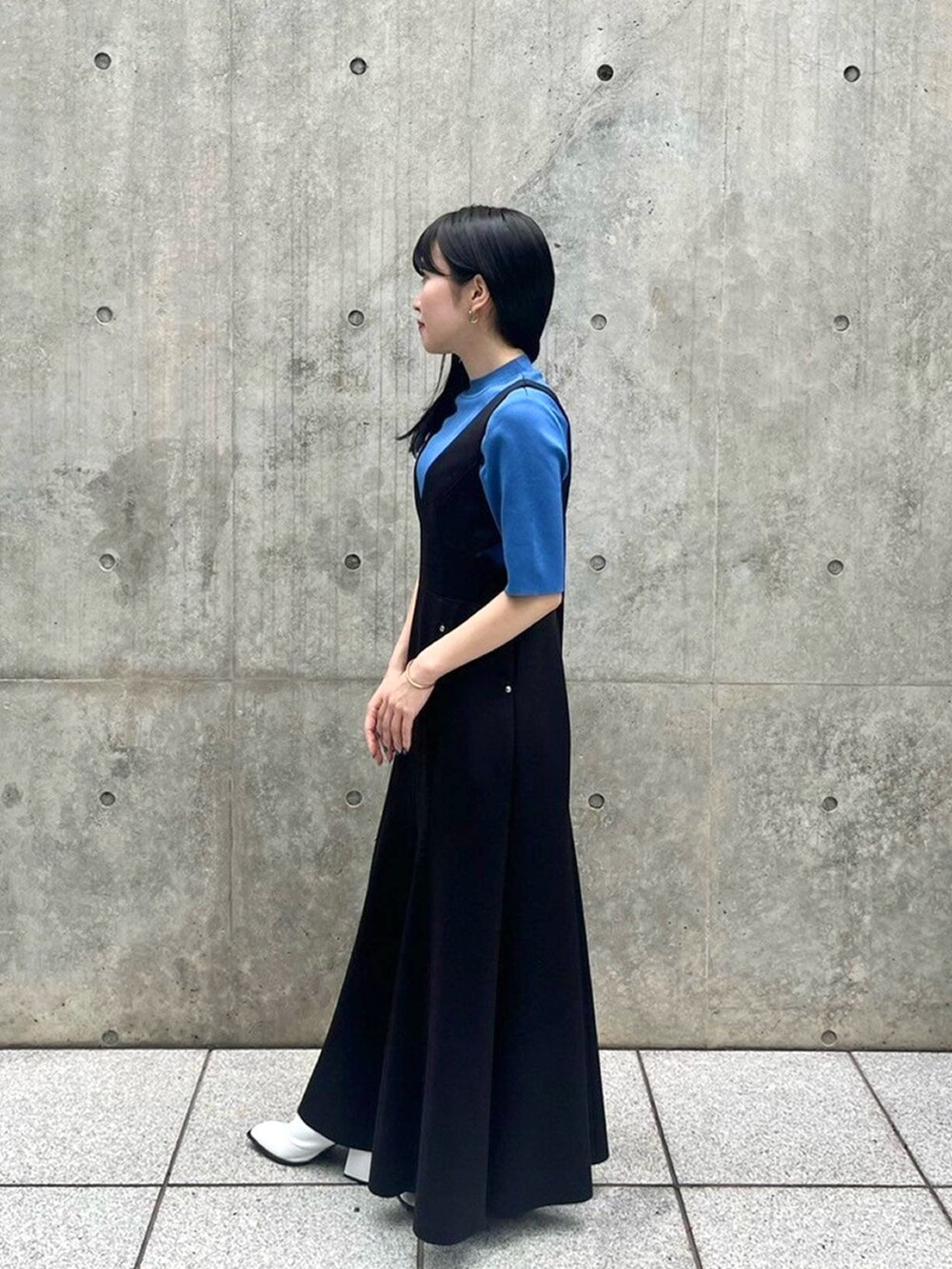 ブルー系のニット/セーター、ブラック系のジャンパースカートを着用したレディースの春コーディネートの2枚目の写真