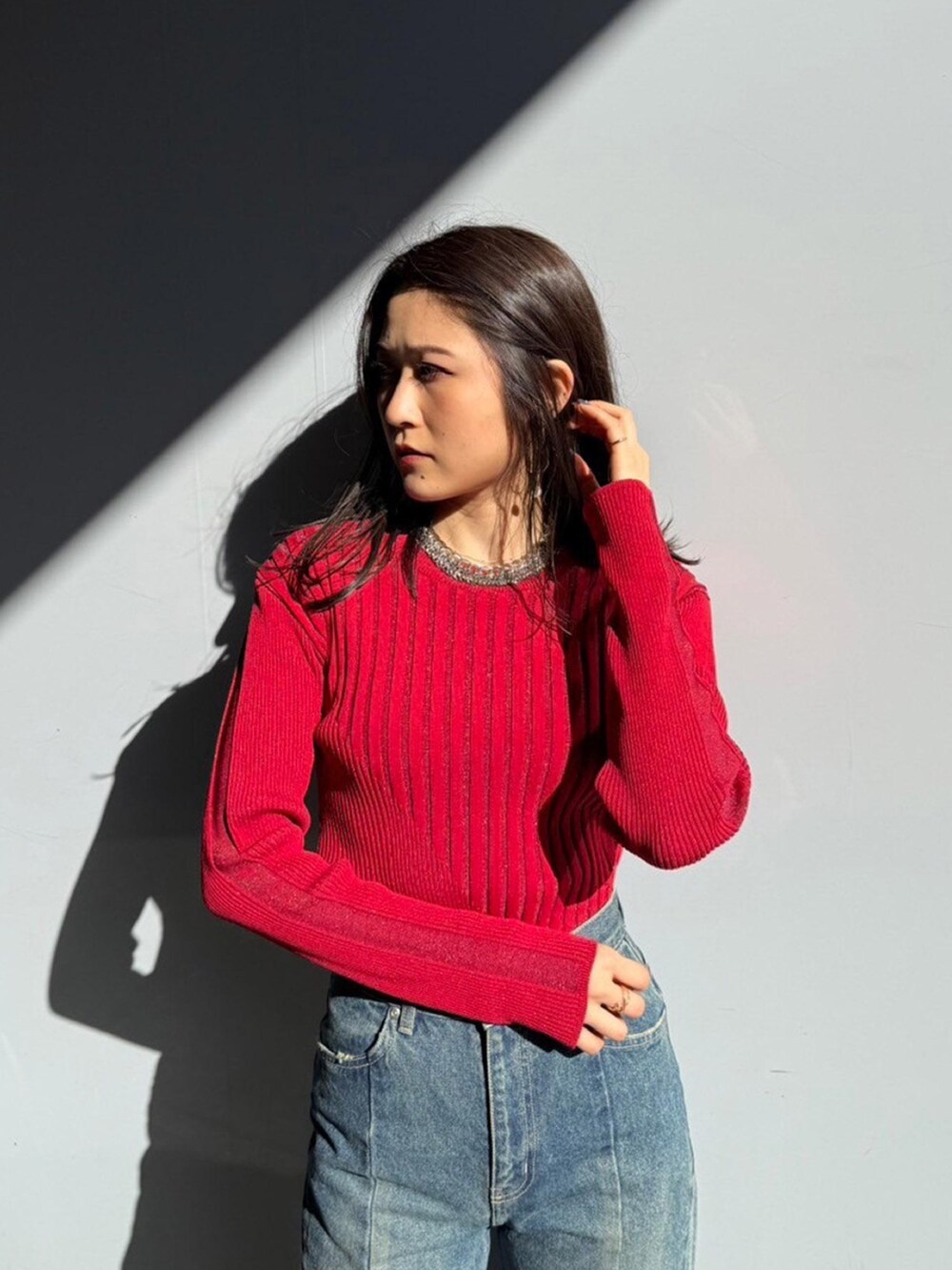 レッド系のニット/セーター、ブルー系のデニムパンツを着用したレディースの秋コーディネートの4枚目の写真