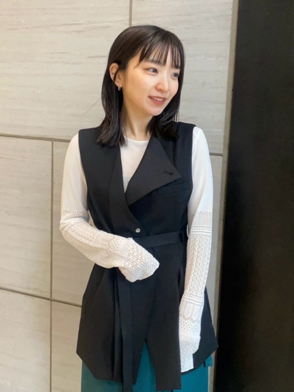 ホワイト系のニット/セーター、ブラック系のベスト、グリーン系のスカートを着用したレディースの春コーディネートの4枚目の写真