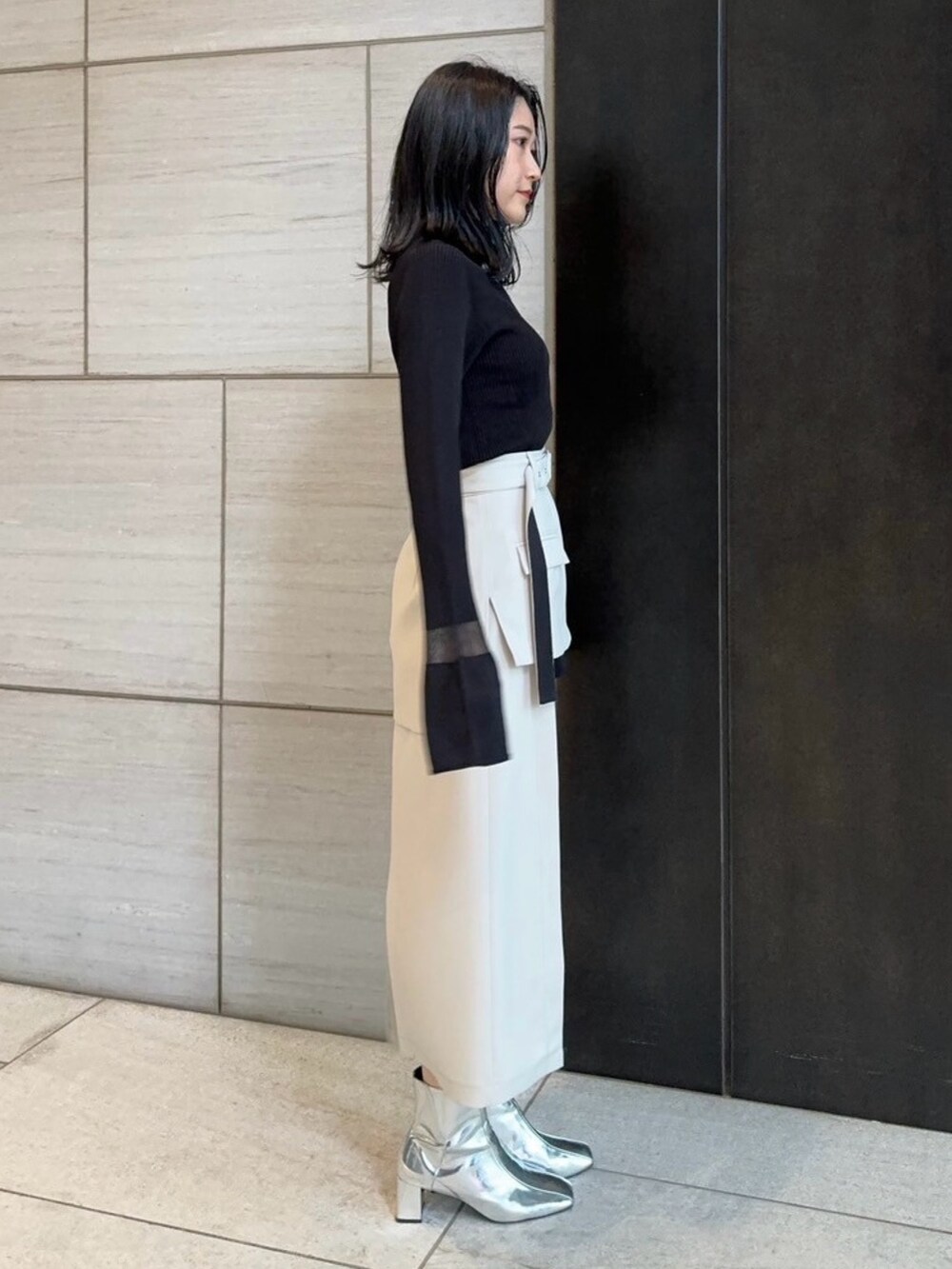 ベージュ系のスカート、ブラック系のニット/セーターを着用したレディースの春コーディネートの2枚目の写真