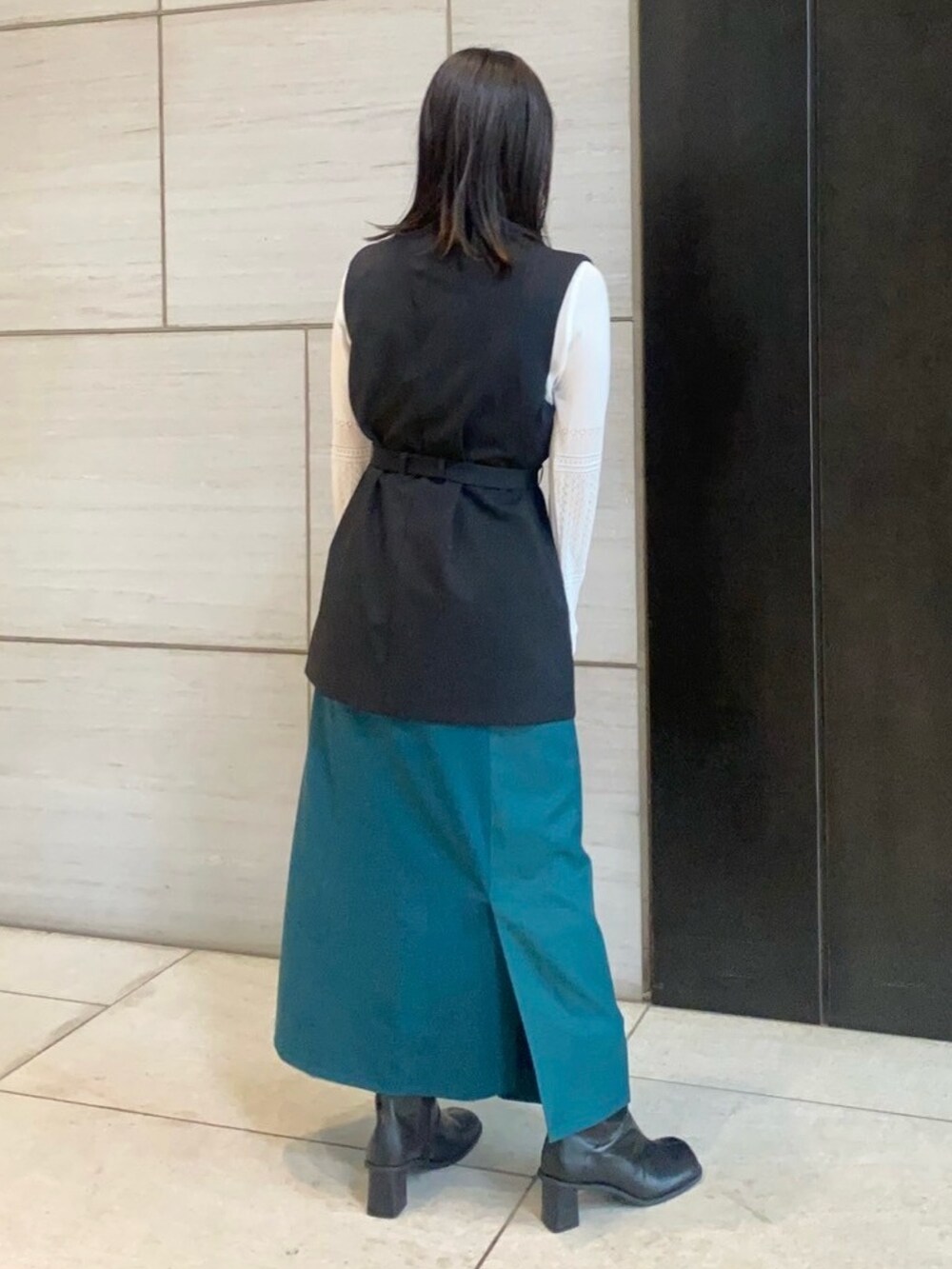 ホワイト系のニット/セーター、ブラック系のベスト、グリーン系のスカートを着用したレディースの春コーディネートの3枚目の写真