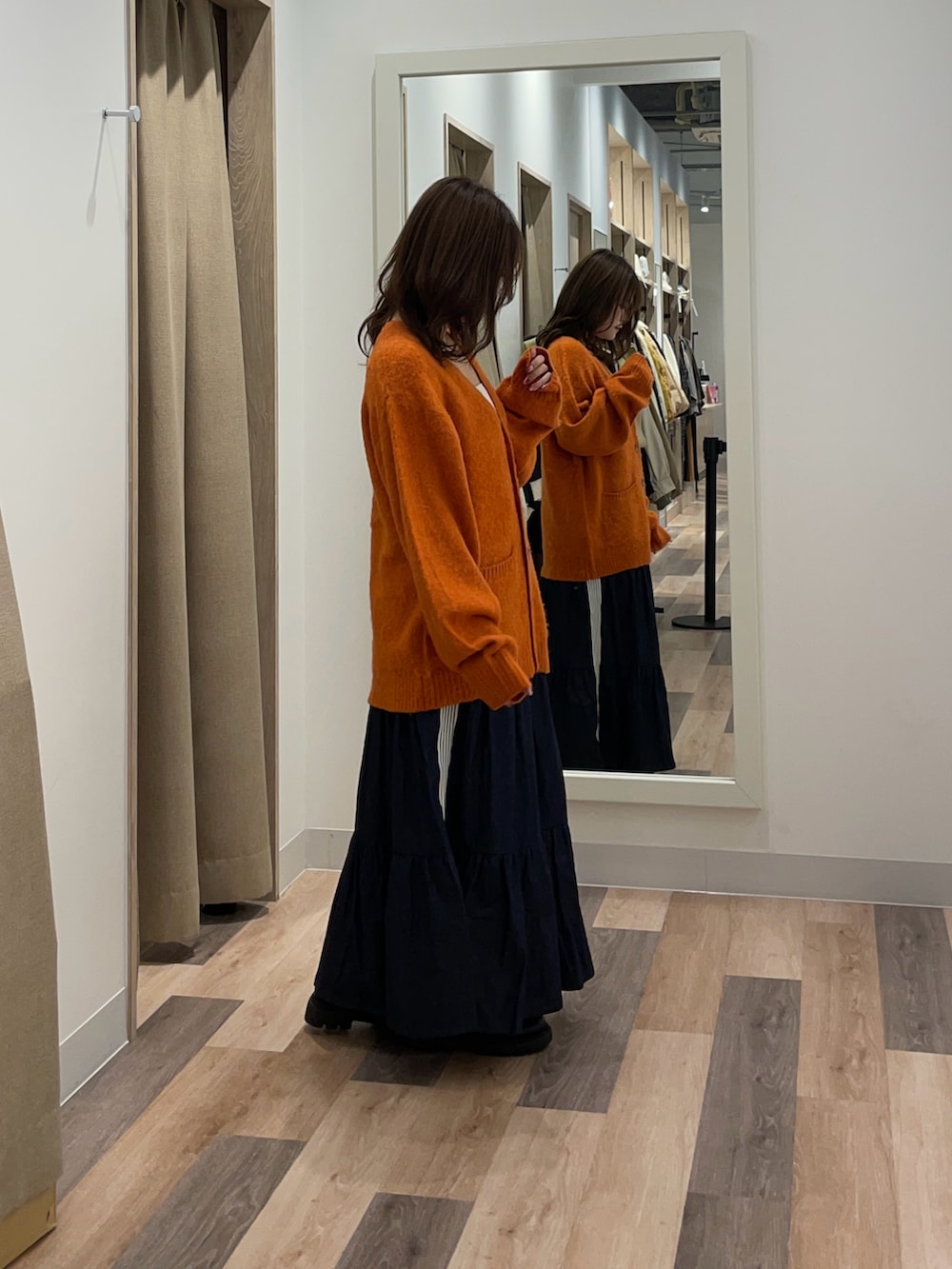 オレンジ系のカーディガン/ボレロ、ブルー系のスカートを着用したレディースの秋コーディネートの2枚目の写真