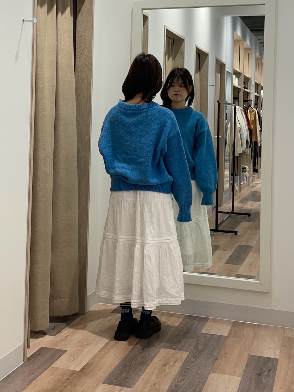 ブルー系のニット/セーター、ホワイト系のスカート、ブラック系のブーツを着用したレディースの秋コーディネートの3枚目の写真