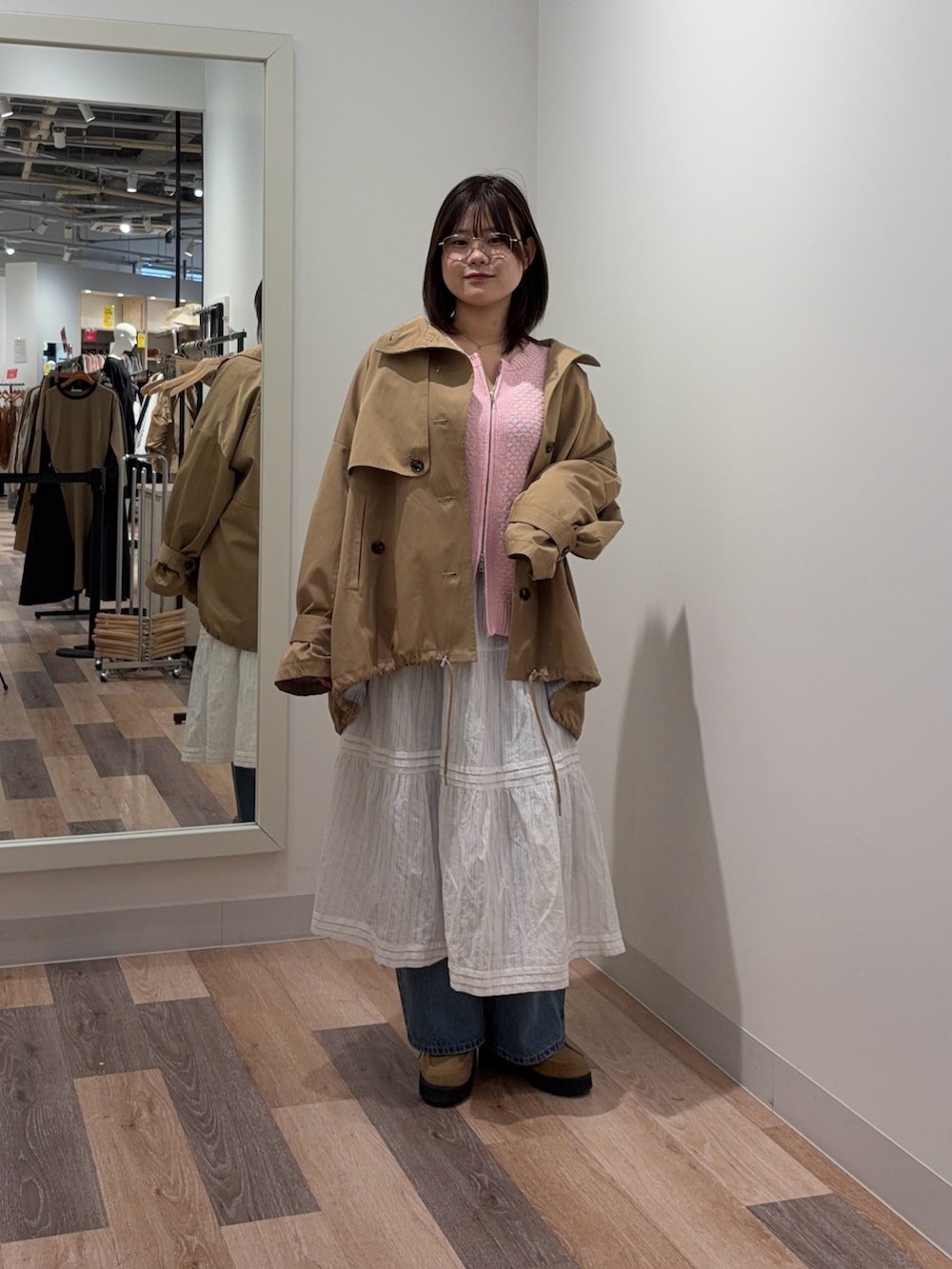 ベージュ系のトレンチコート、ピンク系のカーディガン/ボレロ、ホワイト系のスカートを着用したレディースの冬コーディネートの2枚目の写真