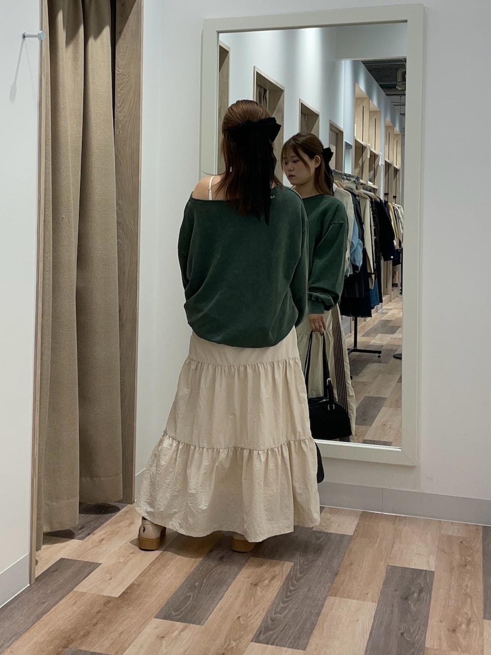 グリーン系のスウェット、ホワイト系のスカート、ブラウン系のボストンバッグを着用したレディースの秋コーディネートの3枚目の写真