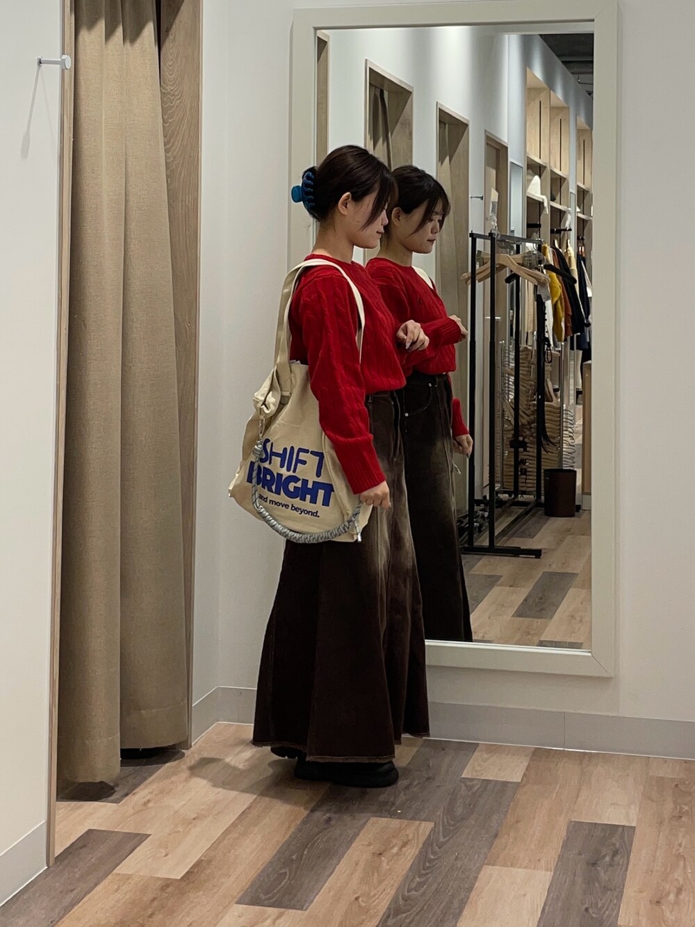 レッド系のニット/セーター、ブラック系のスカート、ホワイト系のトートバッグを着用したレディースの秋コーディネートの2枚目の写真