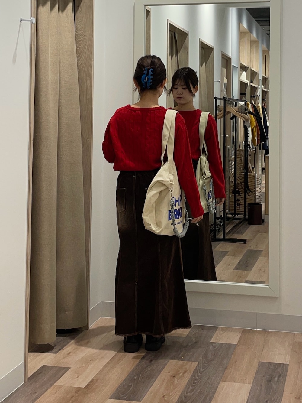 レッド系のニット/セーター、ブラック系のスカート、ホワイト系のトートバッグを着用したレディースの秋コーディネートの3枚目の写真