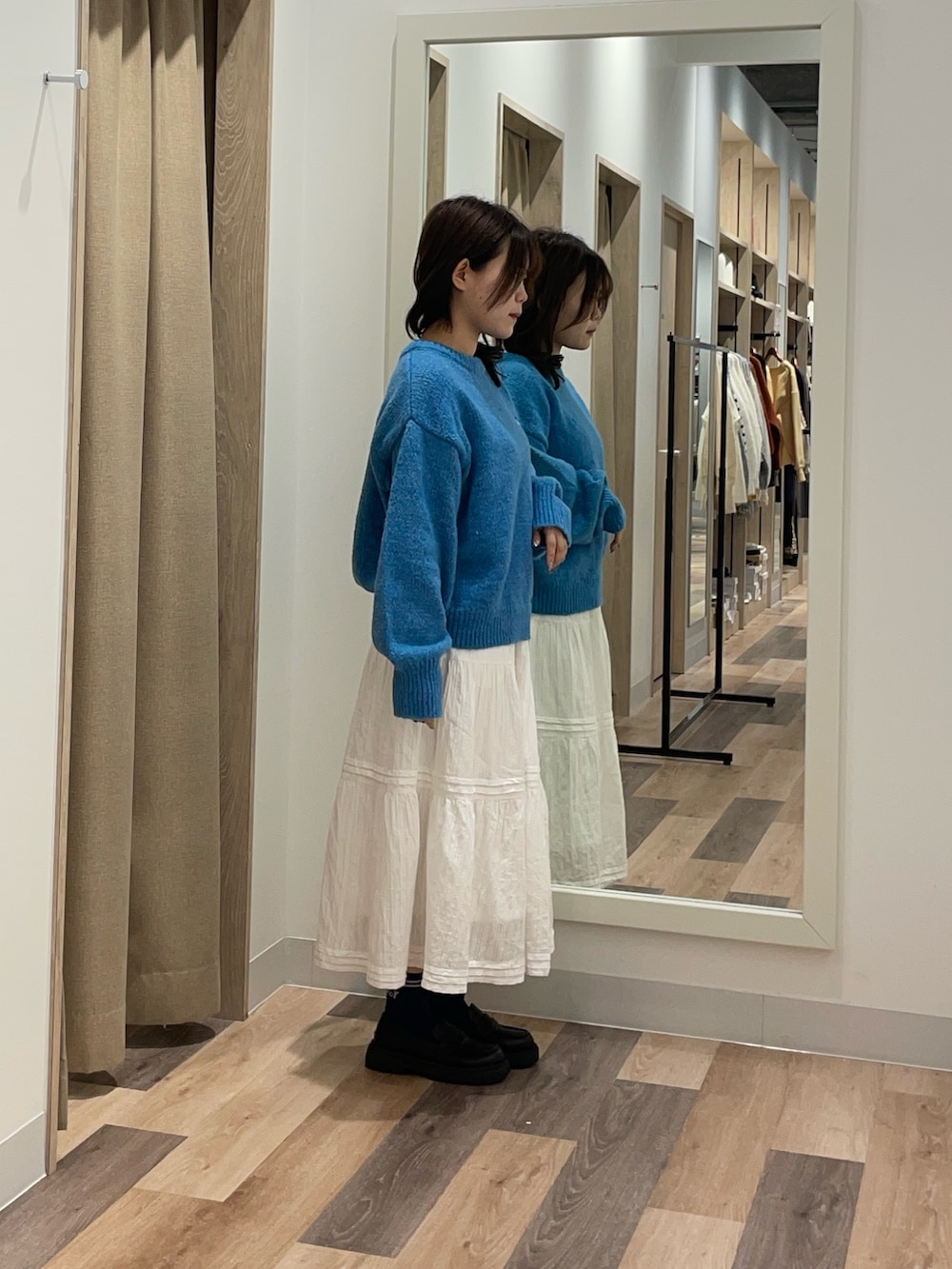 ブルー系のニット/セーター、ホワイト系のスカート、ブラック系のブーツを着用したレディースの秋コーディネートの2枚目の写真