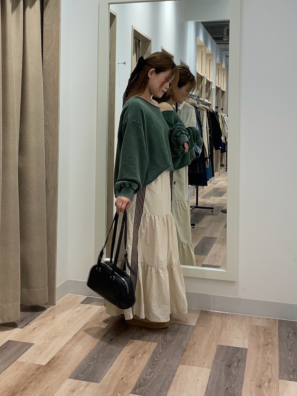 グリーン系のスウェット、ホワイト系のスカート、ブラウン系のボストンバッグを着用したレディースの秋コーディネートの2枚目の写真