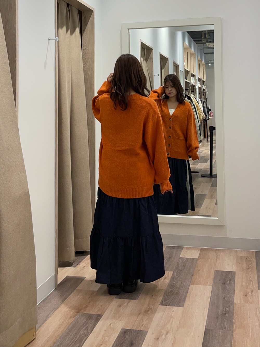 オレンジ系のカーディガン/ボレロ、ブルー系のスカートを着用したレディースの秋コーディネートの3枚目の写真