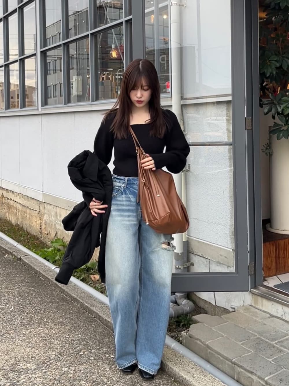 ブラック系のニット/セーター、ブラウン系のショルダーバッグ、ブルー系のデニムパンツを着用したレディースの秋コーディネートの2枚目の写真