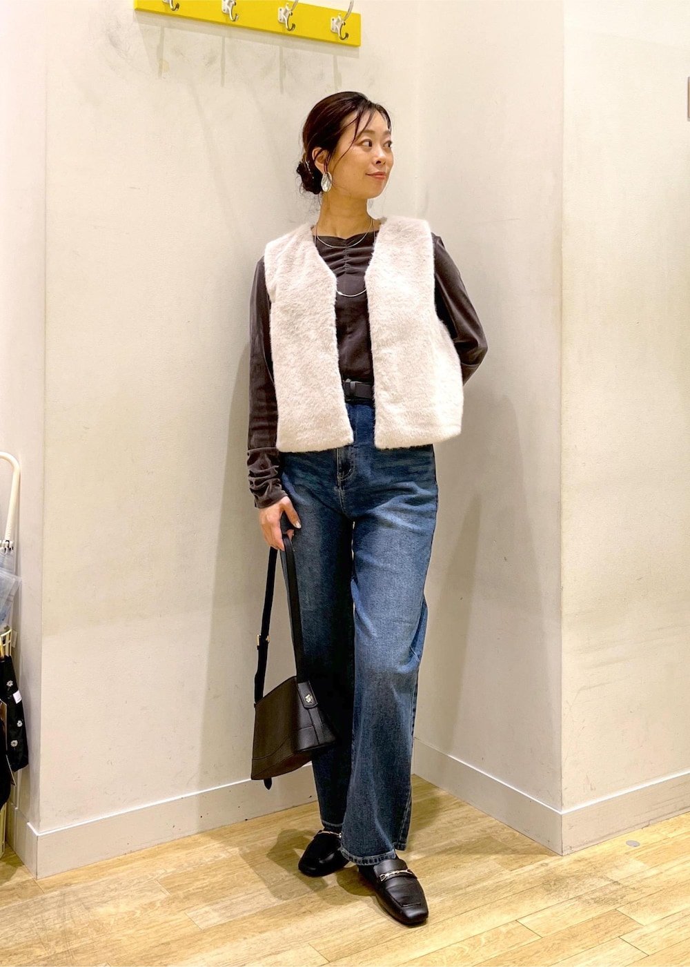 ブルー系のデニムパンツ、ブラック系のショルダーバッグ、ベージュ系のベストを着用したレディースの秋コーディネートの3枚目の写真