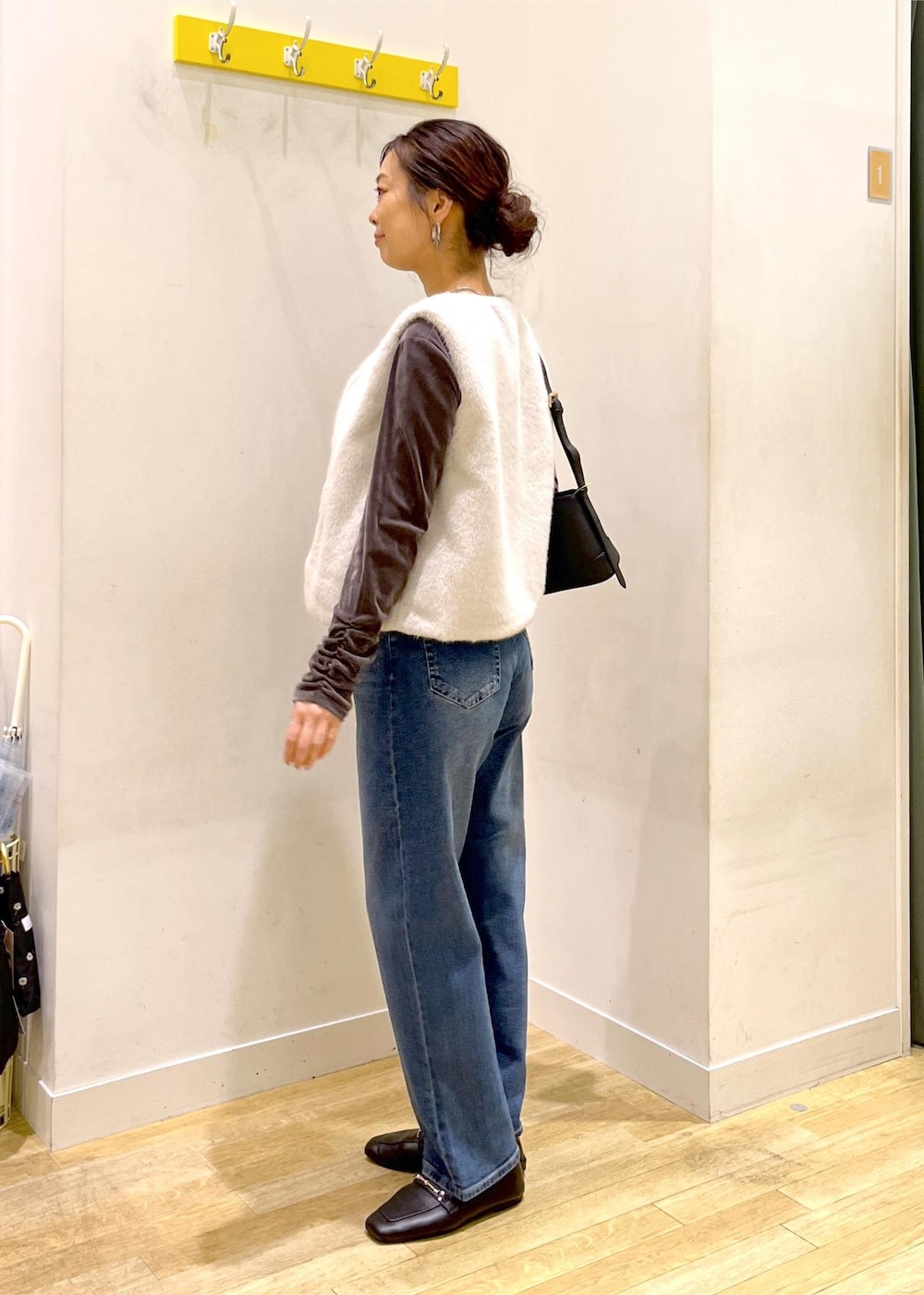 ブルー系のデニムパンツ、ブラック系のショルダーバッグ、ベージュ系のベストを着用したレディースの秋コーディネートの5枚目の写真