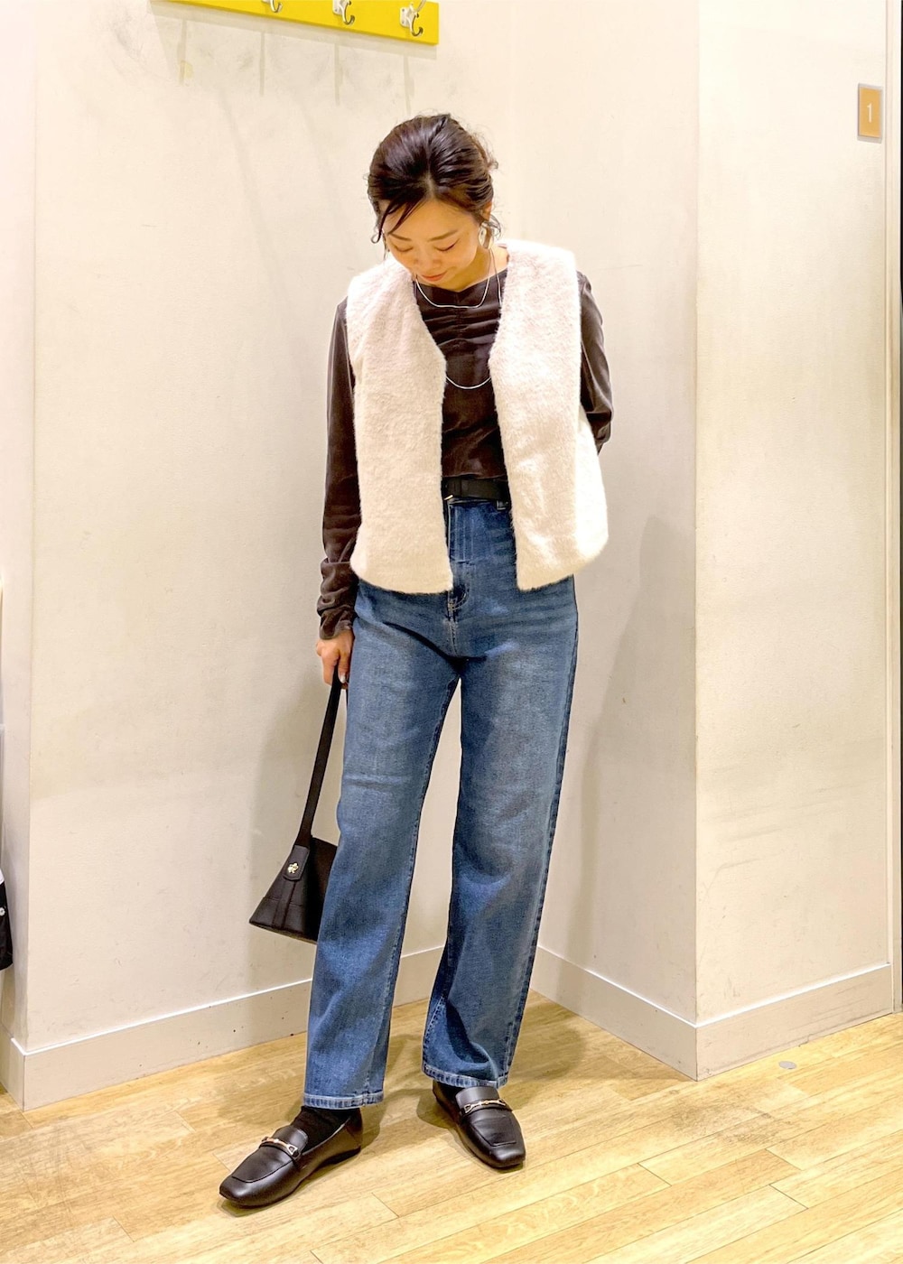 ブルー系のデニムパンツ、ブラック系のショルダーバッグ、ベージュ系のベストを着用したレディースの秋コーディネートの2枚目の写真