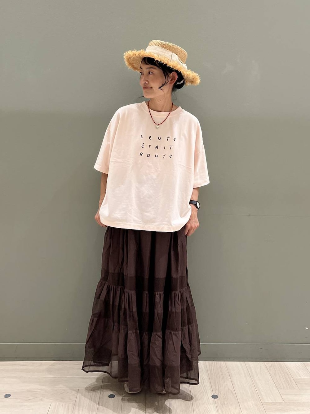 ブラック系のトートバッグ、ピンク系のTシャツ/カットソー、ブラウン系のスカートを着用したレディースの夏コーディネートの2枚目の写真