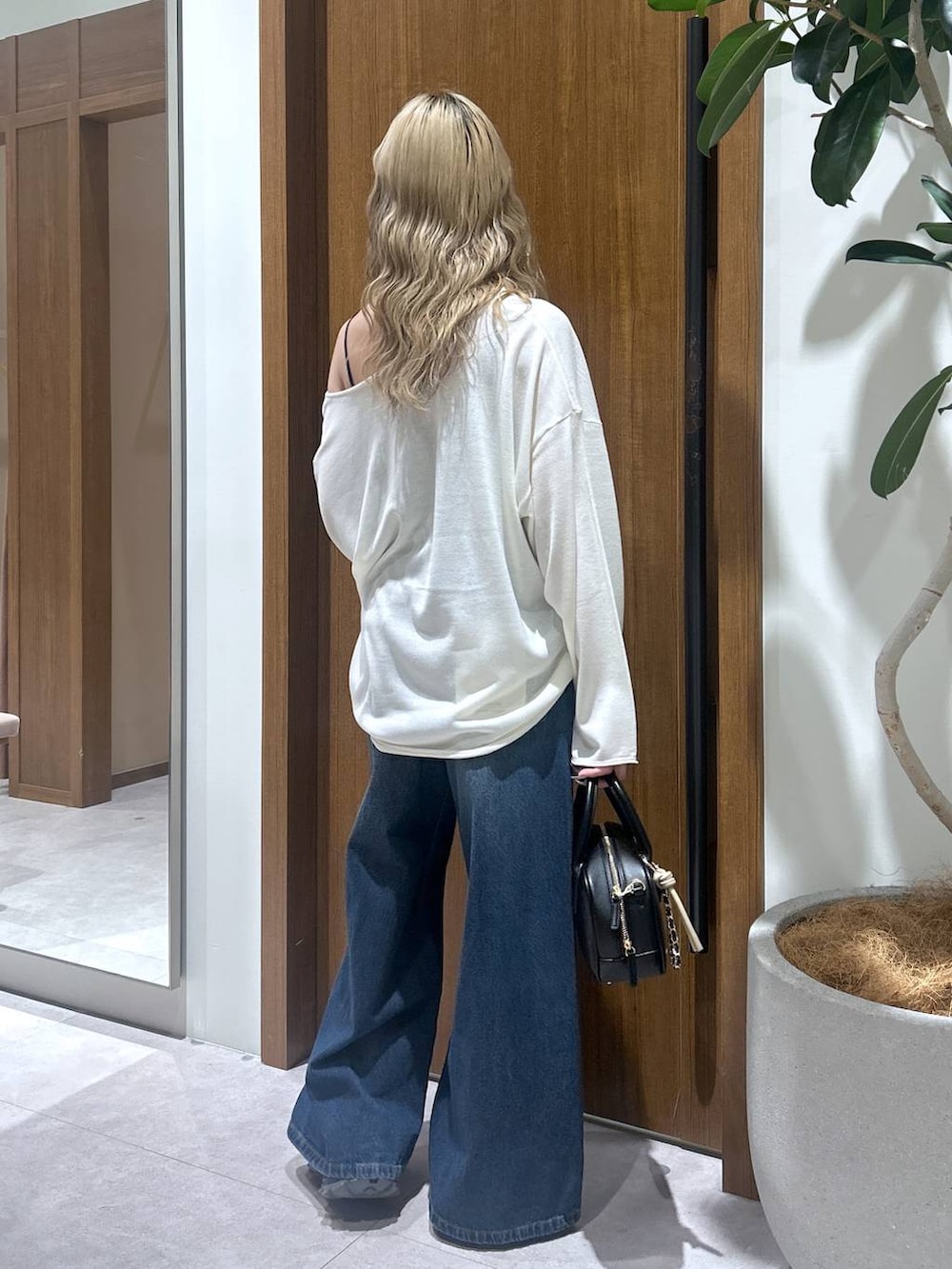 ブルー系のデニムパンツ、ブラック系のハンドバッグ、ホワイト系のニット/セーターを着用したレディースの春コーディネートの3枚目の写真