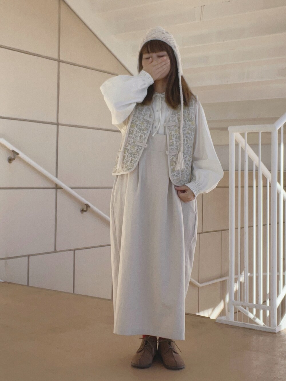 ホワイト系のベスト、ベージュ系のブーツ、ホワイト系のワンピース/ドレスを着用したレディースの冬コーディネートの2枚目の写真